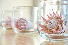 three glass vases with flowers in them sitting on a wooden table next to each other