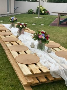 a long wooden table with plates and vases on it in the middle of some grass