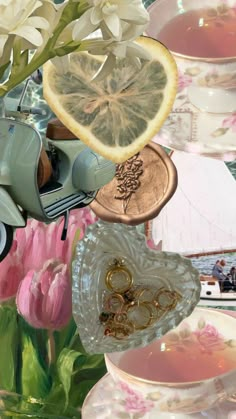 an arrangement of tea cups and saucers with flowers in the background, including lemon slices