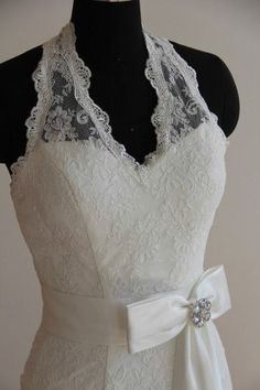 a white wedding dress with lace on the neckline and bow at the waist, tied to a mannequin