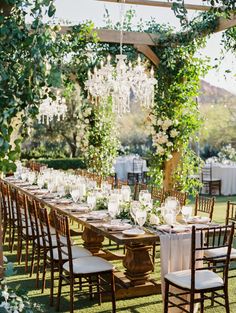 an outdoor dining table set up with chandeliers and white linens on it