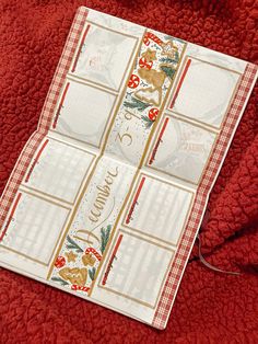 a red blanket with four christmas themed place mats on top of it and a teddy bear sitting in the background