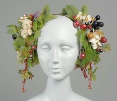 a white mannequin head with flowers and berries on it's forehead, in front of a gray background