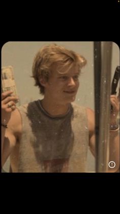 a young man holding two cell phones in front of a mirror