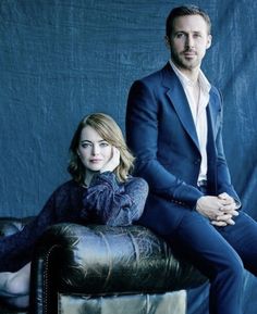 a man and woman sitting on top of a leather chair in front of a blue background