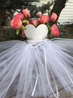 a white vase filled with pink roses on top of a wooden table covered in tulle