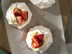 three desserts with whipped cream and strawberries sit on top of a piece of parchment paper