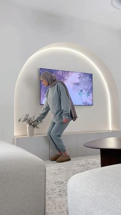 a person in a room with a tv on the wall and a plant near by