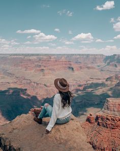 a woman sitting on the edge of a cliff looking out at the canyon below her