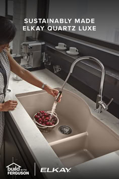 a woman washing strawberries in a sink with the words elkay written above it