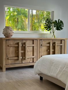 a bed sitting next to a wooden dresser with two windows on it's sides