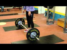 a woman standing in front of a barbell on a gym floor with other equipment