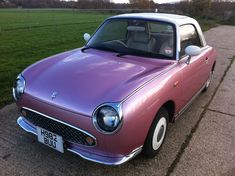 a purple car is parked on the side of the road in front of a grassy field