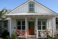 a small white house with a bicycle parked in the front door and two orange chairs on the porch