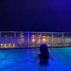 a woman sitting in the middle of a swimming pool at night, looking out to sea