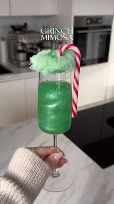 a person holding up a green drink in a wine glass with a candy cane sticking out of it