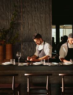 two men in aprons sitting at a table with wine glasses and plates on it