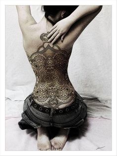 a woman with tattoos on her back sitting on a bed