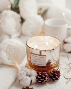 a glass candle sitting on top of a table next to some cotton balls and flowers