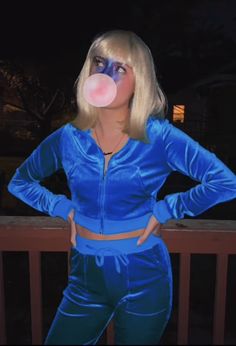 a woman in blue is blowing bubbles on her nose while standing next to a fence