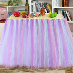 there is a table with a purple and blue tulle skirt on it, along with bookshelves in the background