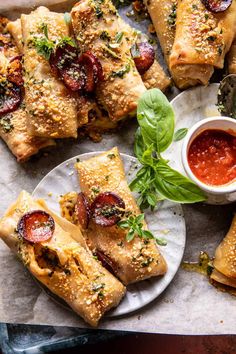 some pizzas are on plates with sauce and herbs next to them, along with other food items