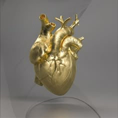 a gold heart sculpture sitting on top of a glass stand in front of a white background