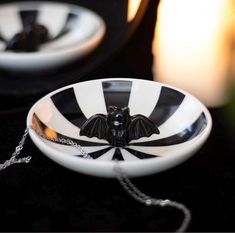 a black and white striped bowl with a bat decoration on the front sits next to a candle