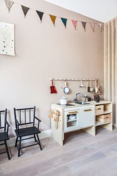 a kitchen area with two chairs and a small stove in the corner, next to a wall hanging flags