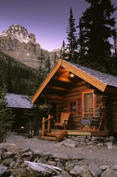 a small cabin is lit up at night with mountains in the background