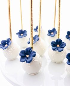 white cake pops with blue flowers and gold sticks in them are on a platter