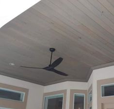 a ceiling fan mounted to the side of a wall in a room with two windows