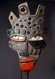 an african mask with holes in it's face on a black stand against a dark background