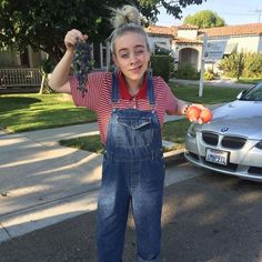 a girl in overalls holding up some fruit