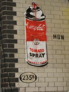 graffiti on the side of a brick building depicting a can of tomato spray painted on it