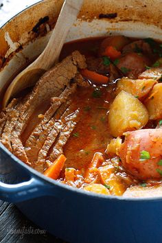 a pot filled with meat and vegetables next to a wooden spoon