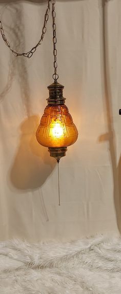 a lamp hanging from a chain on a white wall next to a brown vase with a yellow light in it