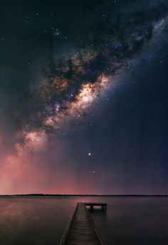 a long dock extends into the ocean under a night sky filled with stars and milky