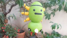 a green stuffed toy hanging from a string in front of some potted plants and trees