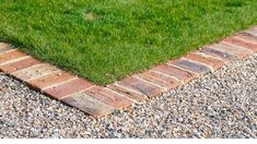 a brick walkway between two green grass lawns on graveled area with small stones