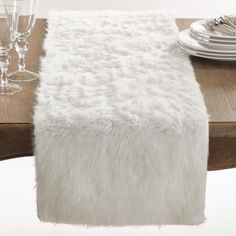 the table is set with silverware and white fur on it, along with wine glasses