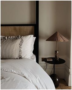 a bed with white sheets and pillows next to a lamp on a table in a bedroom