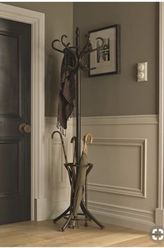 an umbrella stand in front of a door with two coats hanging from it's hooks