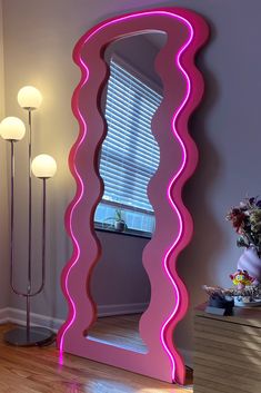 a large pink mirror sitting on top of a hard wood floor next to a lamp