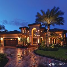 a large house with palm trees in the front yard and lights on it's windows