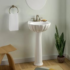 a white pedestal sink in a bathroom next to a potted plant and towel rack