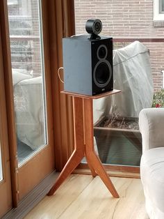 a speaker sitting on top of a wooden stand in front of a window next to a white chair