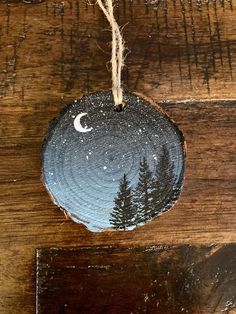 an ornament hanging from a rope on top of a wooden table with pine trees