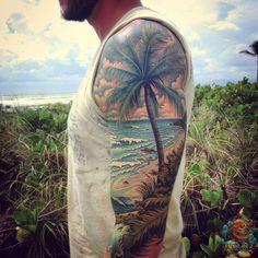 a man with a palm tree and ocean scene on his arm is standing in the grass