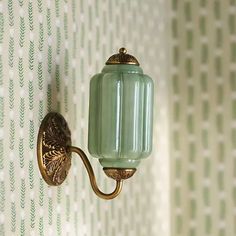 a green glass light fixture on a wall next to a patterned wallpapered wall